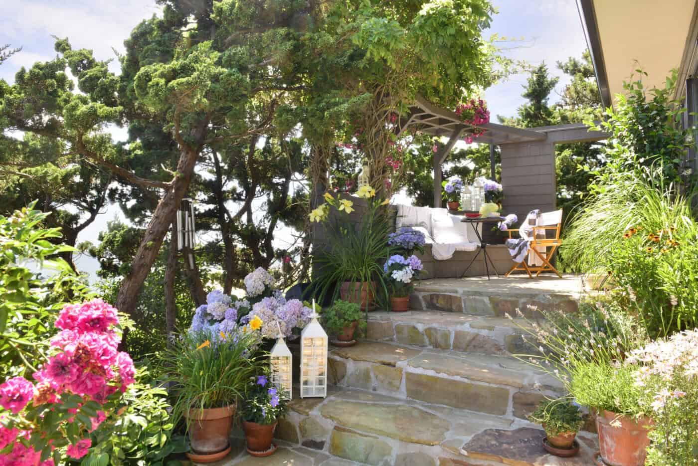 Lush flowers and hardy artifacts line a set of stone stairs. The stone carries to the interior of the house, blurring boundaries between inside and out.